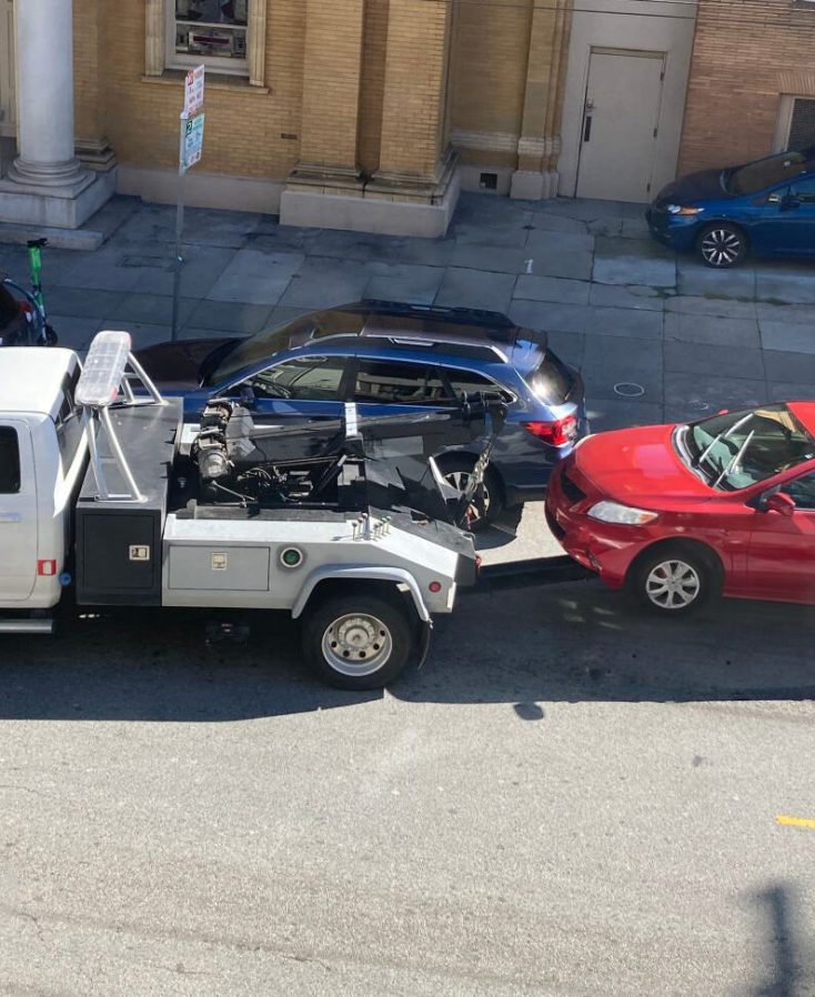 A red sedan is being towed by a white tow truck on a street in San Francisco, California.